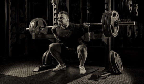 The weightlifter is getting ready to stand with a heavy barbell. Is at the bottom point