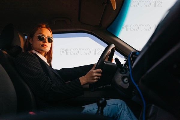 Young beautiful stylish girl driver in a jacket and sunglasses driving a car