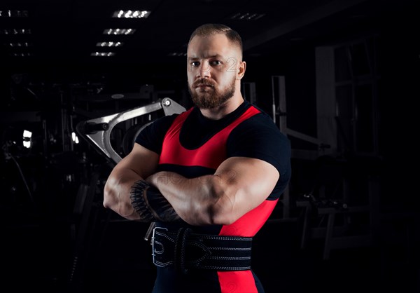 The weightlifter stands in a menacing pose with crossed huge arms and looks at the camera