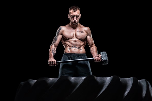 Professional sportsman stands with a sledgehammer in front of a rubber wheel. Functional training concept.