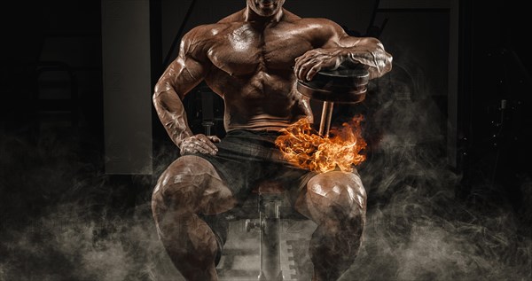 Muscular man sits on a bench with dumbbells burning. Bodybuilding and powerlifting concept.