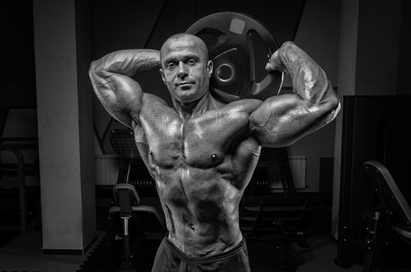 Muscular man posing in the gym with a barbell disc. Bodybuilding and powerlifting concept.