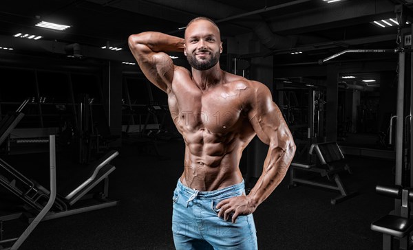 Muscular man in jeans poses in the gym. Sports