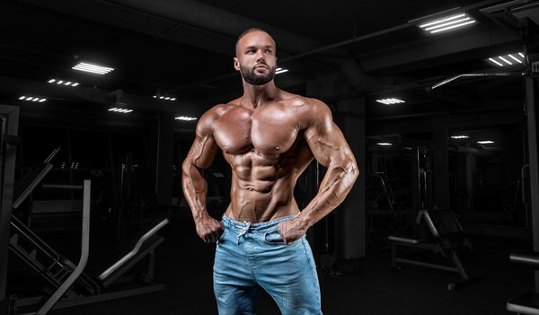 Muscular man in jeans poses in the gym. Sports