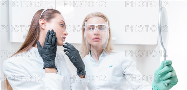 Two beauticians pose in a medical salon with a mirror in their hands. Rejuvenation concept.