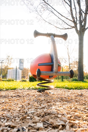 Orange spring rocker for children on a playground near a tree