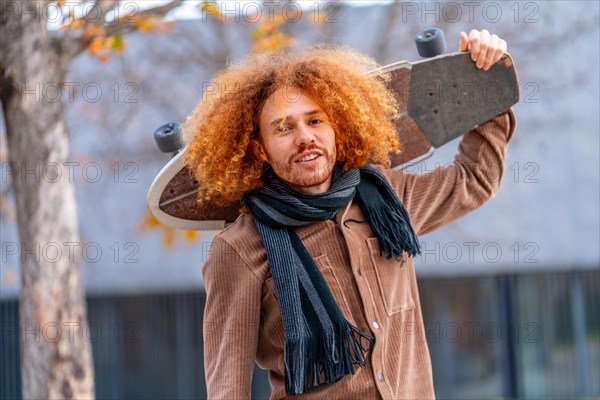 Cool man with curly redhead hair carrying a skateboard in the city