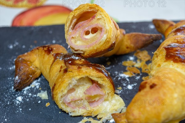 Croissant cut open revealing layers and ham and cheese filling with a shiny glaze