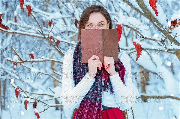 The girl walks through the winter forest. She covered her face with a book. Learning concept. Winter's tale.