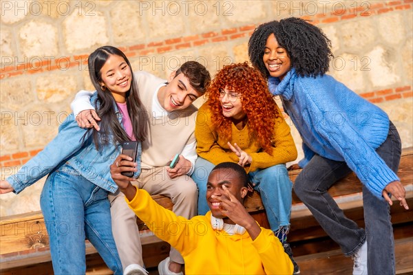 Cool diverse group of teen friends taking a selfie together sitting on a wooden bench outdoors