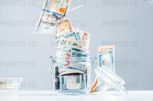 Glass piggy bank full of money. Banknotes are strewed from above. The concept of squandering.