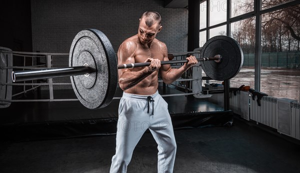 Handsome young man working out with a barbell in the gym. Biceps pumping. Fitness and bodybuilding concept.