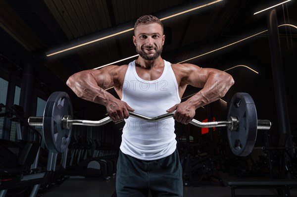 Handsome young man working out with a barbell in the gym. Shoulder pumping. Barbell pull to the chin. Fitness and bodybuilding concept