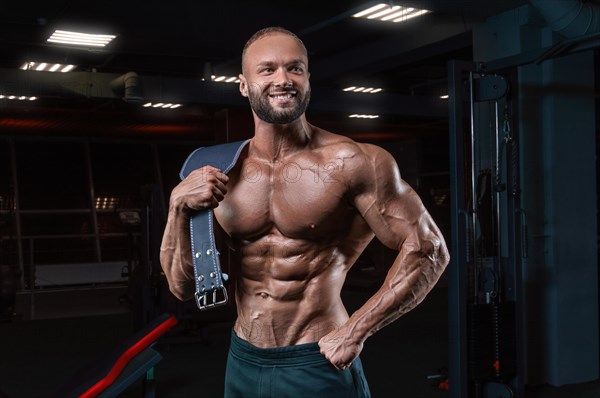 Muscular man poses in the gym with an athletic belt. Sports