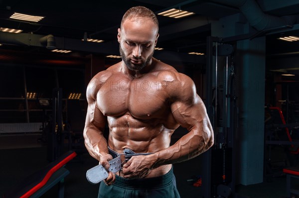 Muscular man poses in the gym with an athletic belt. Sports