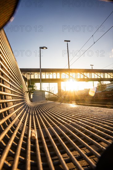 View along a metal grid of a bench onto an urban bridge architecture at sunset