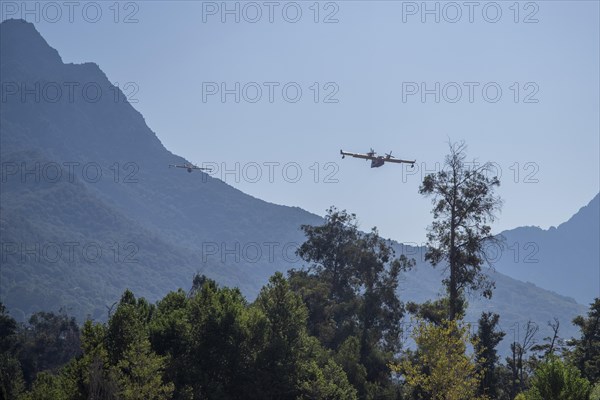 Two fire-fighting aeroplanes flying in formation over a forest near the mountains