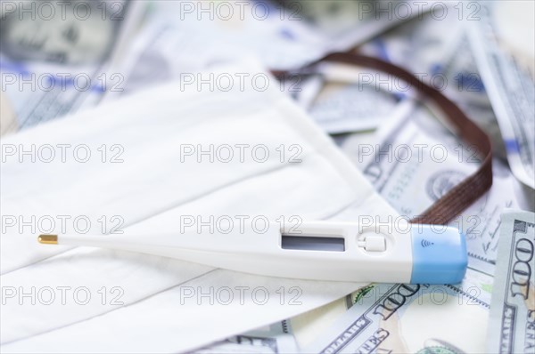 Medical mask and a thermometer lie on one hundred dollar bills. The concept of an epidemic