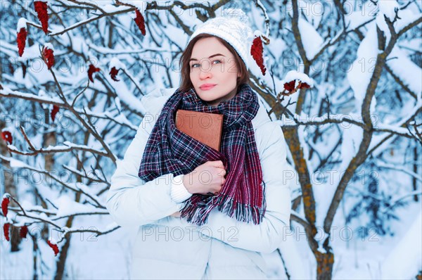 The girl walks through the winter forest. She covered her face with a book. Learning concept. Winter's tale.