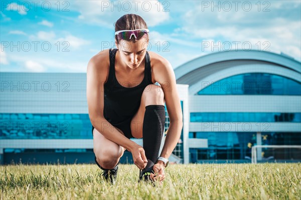 Portrait of a young runner who laces her boots at a football stadium. Sports concept.