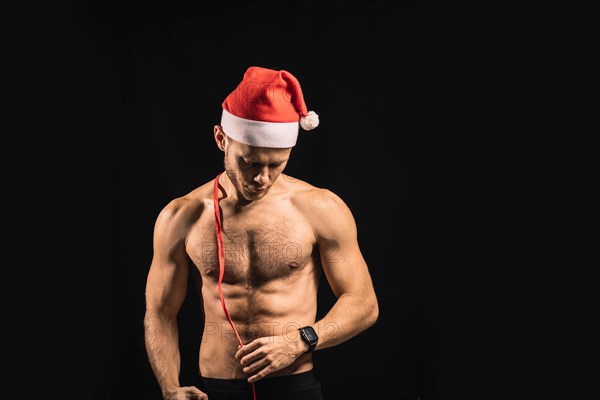 Sexy athletic man with a naked torso in a santa claus hat is preparing for a performance for christmas