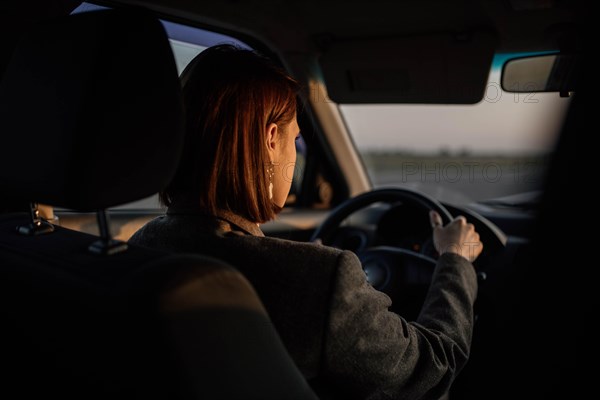 Young beautiful smiling woman taxi driver in a jacket sits behind the wheel of a car