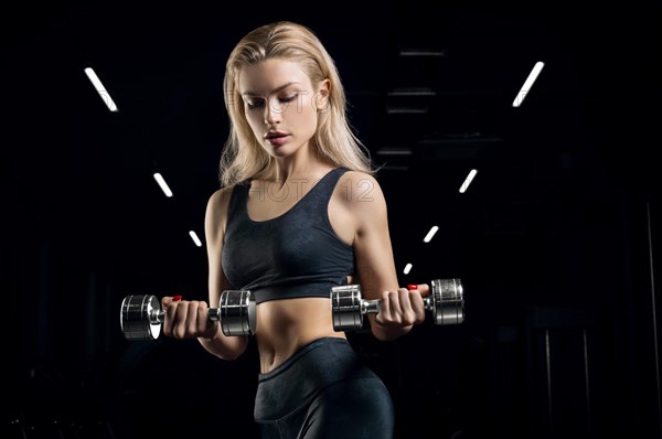 Charming sportswoman posing in the gym with dumbbells. The concept of bodybuilding