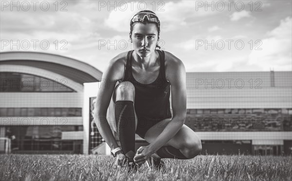 Portrait of a young runner who laces her boots at a football stadium. Sports concept.