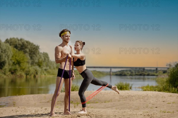 Young athletic couple doing exercise with resistance band on the shore of a lake on a sunny day