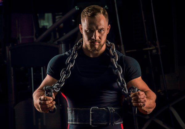 Handsome athlete with a chain around his neck stands in the gym and looks straight ahead