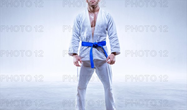 Athlete in a kimono with a blue belt stands on a light background. The concept of karate and judo.