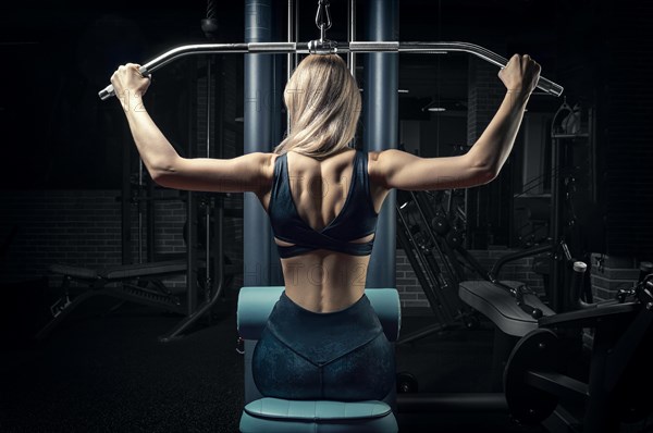 Charming blonde does exercises for the back in the gym. Neck pull for the head. The concept of sports