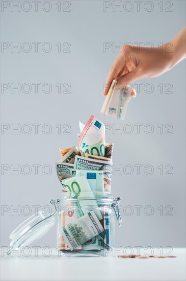 Female hand puts a bill into a glass piggy bank full of money. Thrift concept.