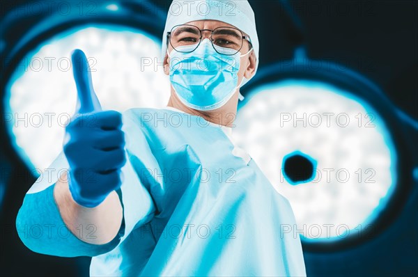 The doctor against the background of surgical lamps shows a raised finger. Medicine concept.