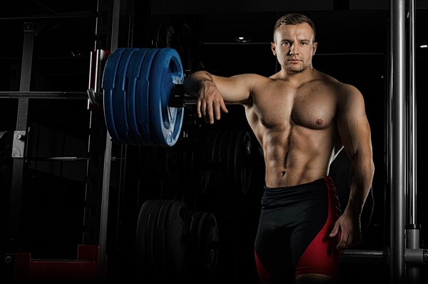 The weightlifter leans his hand on the barbell and looks menacingly forward. Front view