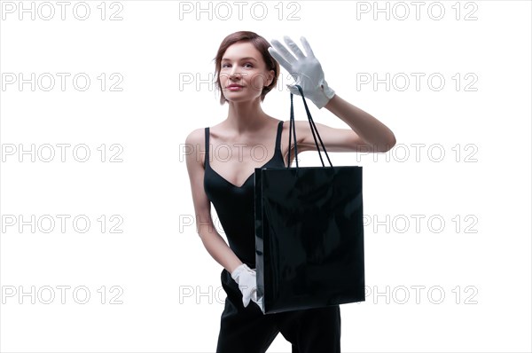 Beautiful young woman in white gloves holds a black craft bag in her hand. Shopaholics concept. Spenting. Gifts for the holidays. Black Friday. Shopping centers.