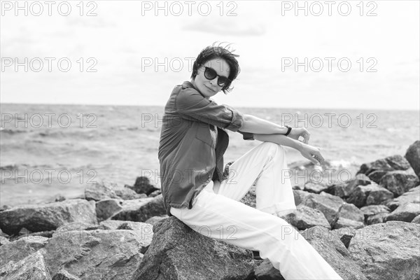 Portrait of a stylish woman sitting on stones in the bay. Windy weather. Happiness
