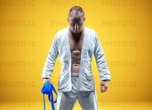 Strong man in a kimono with a blue belt. Yellow background. Martial arts concept.