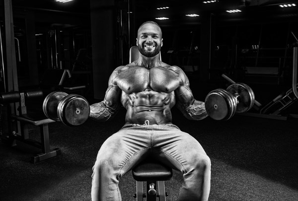 The athlete is doing the exercise in the gym. Lifting dumbbells while sitting on a bench. Fitness