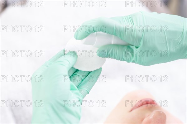 Image of hands in green gloves holding a spray bottle and cotton pads. Skin care concept.