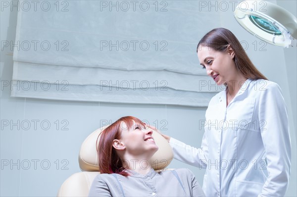 Beautician consults a woman in a beauty salon. The patient sits in a cosmetic chair and smiles at the specialist.