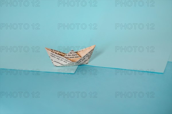 An origami paper boat on a two-tone background casting a long shadow