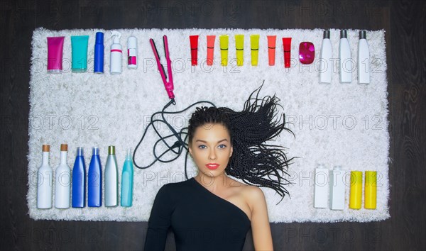 Charming girl lies on a snow-white carpet. Against the background lie cosmetic means for hair care