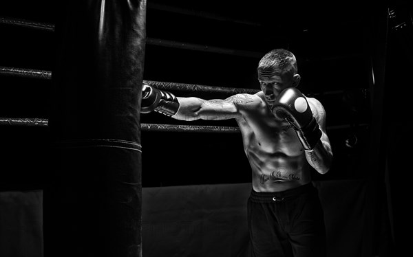 Professional boxer hits the bag against the background of the ring. Side view. The concept of sport and classic boxing.