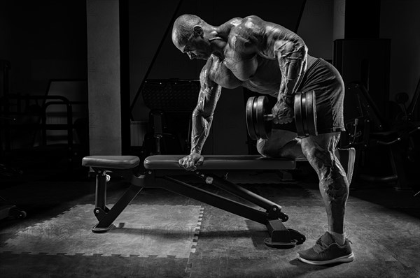 Muscular man pulls a dumbbell towards his stomach. Bodybuilding and powerlifting concept.