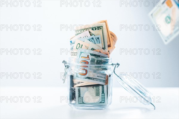 Glass piggy bank full of money. Banknotes are strewed from above. The concept of squandering.