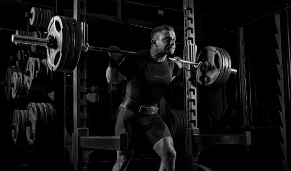 The weightlifter is preparing to lift a very heavy barbell. He exhales breathlessly and strains as much as possible before performing the exercise