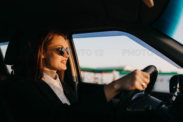 Young beautiful stylish girl driver in a jacket and sunglasses driving a car