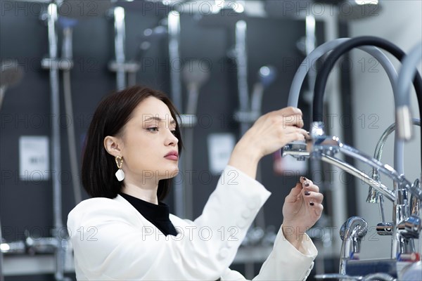 Beautiful young woman in a white jacket chooses plumbing supplies in a hardware store