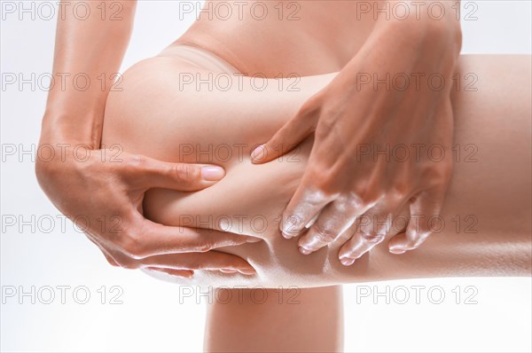 Image of a woman squeezing the skin on her thigh. Cosmetic concept.